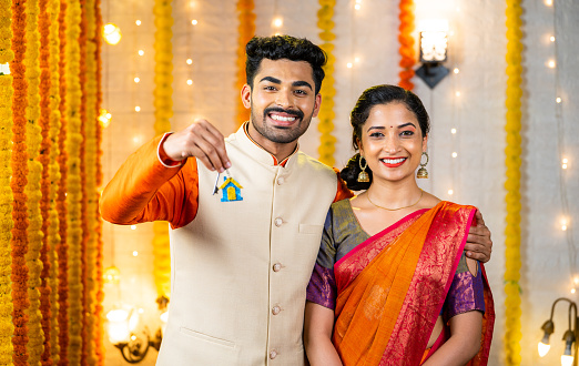 Happy young indian couple showing new home keys by looking at camera home - concept of new festival purchase, investment planning and family relationship.