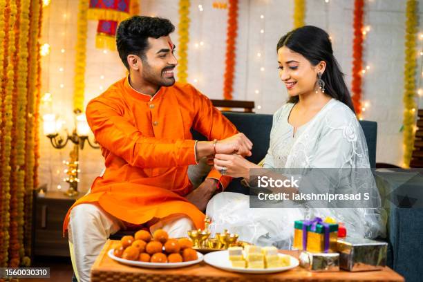 Happy Young Indian Girl Tying Rakhi To Brother Hand During Raksha Bandhan Festival At Home Concept Of Indian Culture Relationship And Occasion Stock Photo - Download Image Now