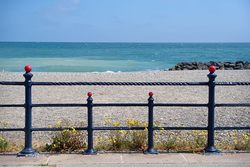 Seascape with the Irish Sea and pebble beach seen through symmetrical metal railings of the promenade in Bray, Ireland.