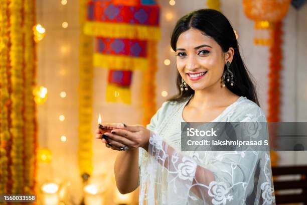 Happy Indian Girl Looking At Camera By Holding Diya Lamp During Diwali Festival Celebration On Decorated Background Concept Of Traditional Culture Greetings And Spirituality Or Harmony Stock Photo - Download Image Now