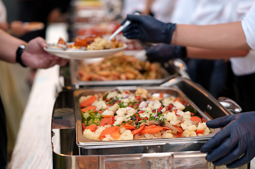 The concept of a culinary buffet dinner catering comes to life as a group of people gather in a restaurant, enjoying an all-you-can-eat spread of meat, vegetables, and other delectable food options.
