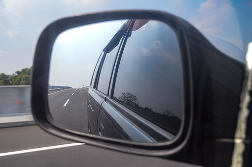rearview mirror view of a car traveling at high speed on a toll road