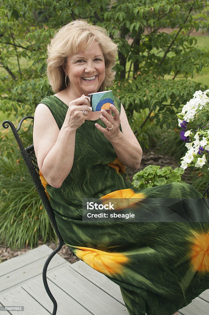Cheerful older woman holds a coffee mug. A cheerful older woman is enjoying her morning coffee on the back deck. 60-64 Years Stock Photo