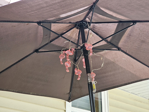 Some pink flamingo lights hung up under an umbrella.
