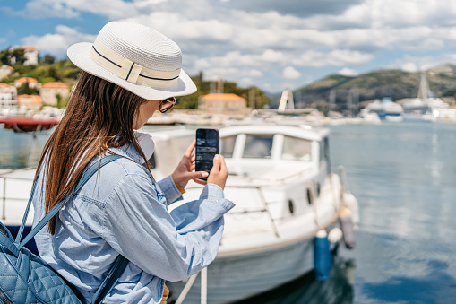 Young female tourist taking a picture of a boat in Dubrovnik bay in Croatia.