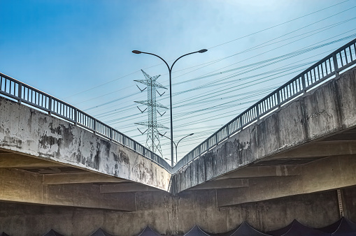 branching of a pedestrian bridge or flyover bridge with a street lighting pole in the middle against a backdrop of high-voltage power towers and a clear blue sky during hot weather