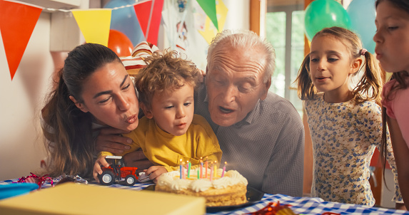 Portrait of a Small Family Gathering Around a Birthday Cake to Blow Out Candles. Family Members Throwing a Party to Celebrate Their Grandfather's Birthday. Cute Kids, Mother and Senior Man Gathering