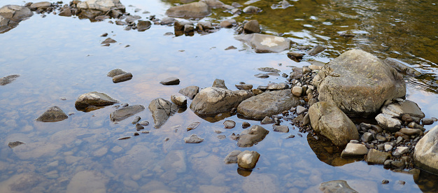 Rocky stream bed. The stream bed is filled with water and the water is clear. The rocks are various sizes and colors, ranging from small pebbles to larger boulders.