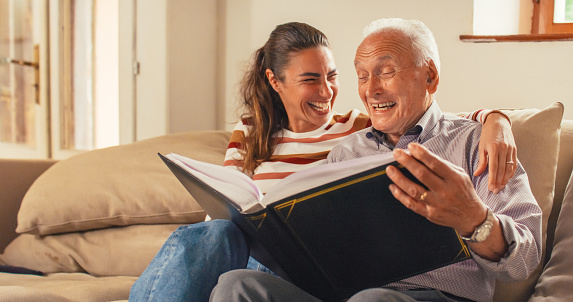 Portrait of a Nostalgic Woman Bringing the Family Photo Album to her Senior Father so They Can Watch Photos Together. Old Man Sharing Funny Memories and Stories with his Daughter