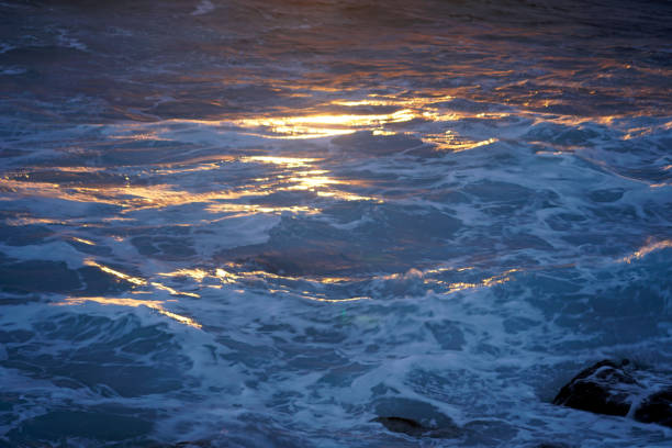 Golden sunset reflecting on the surface of the ocean, creating a beautiful contrast with the dark blue of the moving waves at punta faxilda