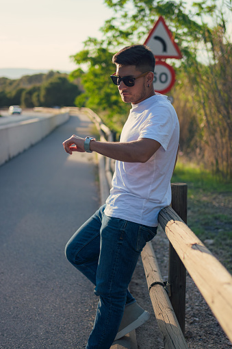 Latino man in sunglasses looks at his watch on the side of the road