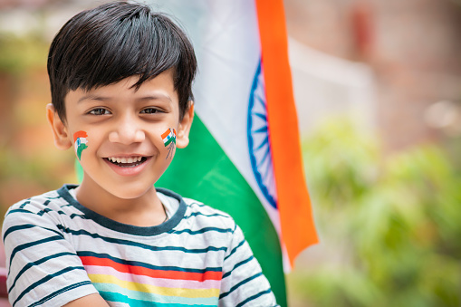 Portrait of an Indian boy celebrating independence day with Indian flag sticker on face. He is looking at the camera with a toothy smile.