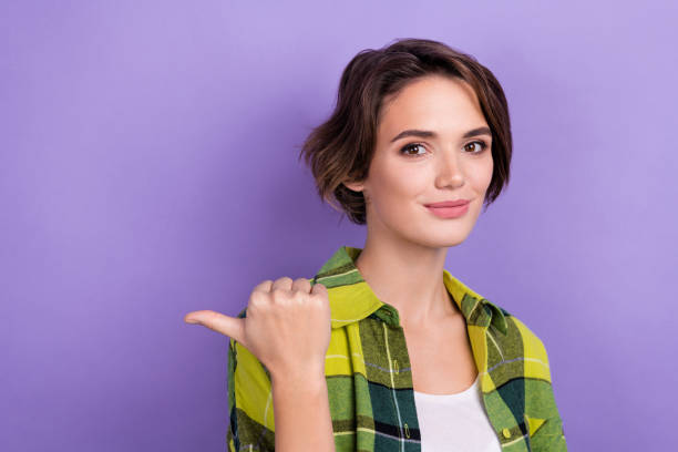 istock Portrait of friendly lovely lady indicate thumb finger empty space ad proposition blank isolated on purple color background 1560187328