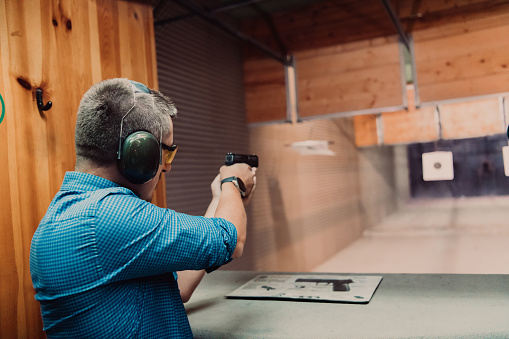 A man practices shooting a pistol in a shooting range while wearing protective headphones.