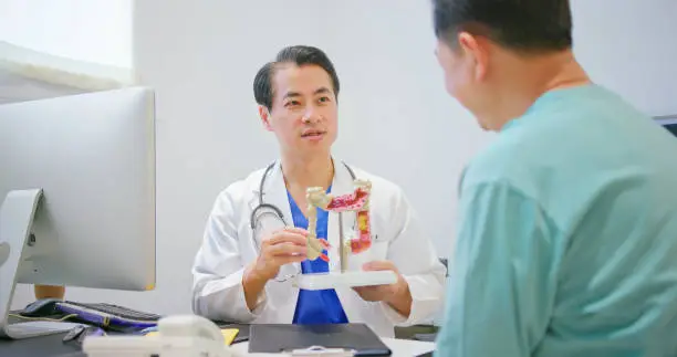 colorectal cancer concept - asian senior male doctor is showing large intestine model and explaining to elder man patient in hospital