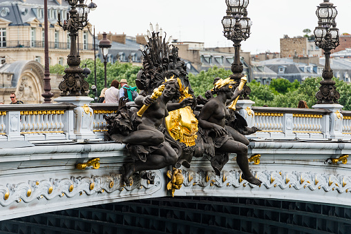 Paris, France - May 20, 2023: The Nymphs of the Seine on Pont Alexandre III. The Pont Alexandre III is a deck arch bridge that spans the Seine in Paris. It connects the Champs-Élysées quarter with those of the Invalides and Eiffel Tower. The nymph reliefs are at the centres of the arches over the Seine, memorials to the Franco-Russian Alliance. The Nymphs of the Seine has a relief of the arms of Paris, and faces the Nymphs of the Neva with the arms of Imperial Russia. They are both executed in hammered copper over forms by Georges Récipon.