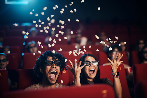 Surprised diverse couple having fun while watching a 3D comedy movie in theatre.