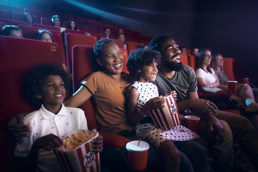 Happy African American family enjoying while watching a movie in cinema.