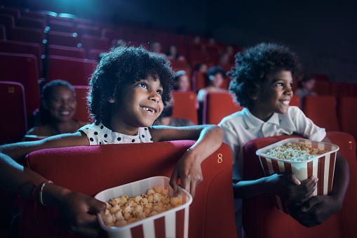 Happy African American siblings watching a cartoon in movie theatre.