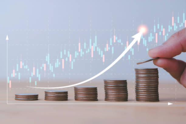 istock Saving money concept with Human hand putting coin stacking with virtual trend graph on wooden table. Business investment growth and profit increase concept. 1560237055