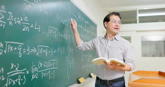 side view asian senior male calculus professor is teaching in front of blackboard at college classroom