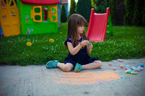 A child is sitting on the ground and playing with chalk. A girl tries to create art with some colorful chalk.