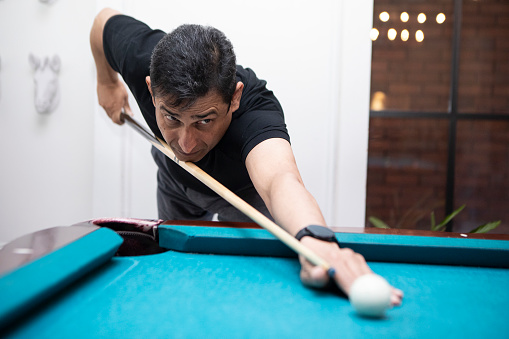 Playing a shot on a turquoise-coloured pool table. The man is wearing a black polo shirt.