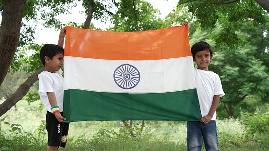 Cute little boys holding Indian flag in their hands and smiling. Celebrating Independence day or Republic day in India. Kid showing pride of Tiranga