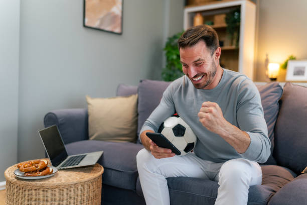istock Happy mature man with soccer ball using smartphone 1560300174