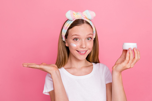 Photo of charming teen girl hold facial cream jar arm demonstrate empty space promo isolated on pink color background.