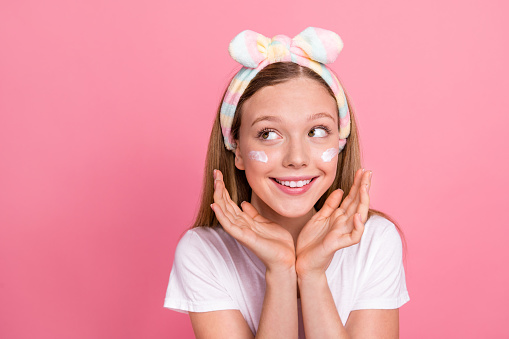 Portrait of adorable sweet girl hands under face apply hydration balm under eyes look empty space isolated on pink color background.