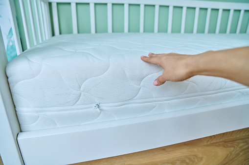 Close-up of woman's hand touches mattress on children baby bed. Female pressing, checking quality of hardness and softness of mattress. Child health, comfortable sleep concept