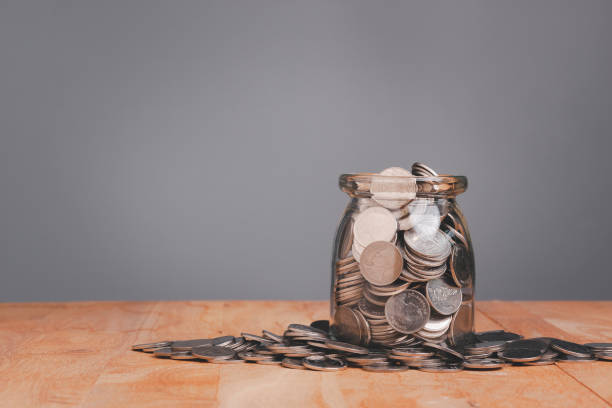 Saving planning with coins in a glass jar on wooden table over gray wall background with Save money concept for Financial Banking Business Ideas, Investments, Funds, Bonds, Dividends and Interest. Saving planning with coins in a glass jar on wooden table over gray wall background with Save money concept for Financial Banking Business Ideas, Investments, Funds, Bonds, Dividends and Interest. deposit bottle stock pictures, royalty-free photos & images