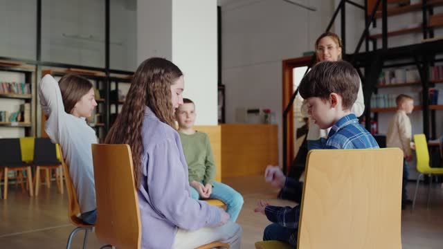 Children play rock paper scissors in class with teacher sitting in circle