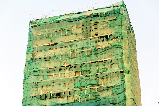 Tall building with bamboo scaffolding, and covered in tattered ripped scaffold netting,  Phnom Penh city, Cambodia