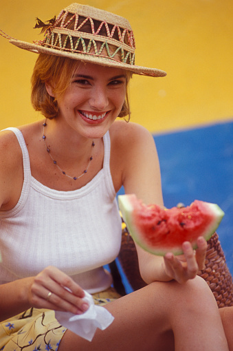 Woman with straw hat eating watermelon on the sidewalk, Venezuela