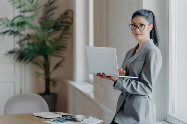 istock Formal administrative woman with modern laptop, using wireless internet, searches info online, working remotely. 1560332975