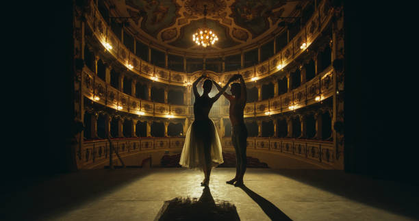 toma cinemática de una joven pareja de bailarines de ballet clásico actuando en el escenario del teatro clásico con iluminación dramática. bailarines y bailarinas ensayan juntos su actuación antes de un espectáculo - ópera fotografías e imágenes de stock