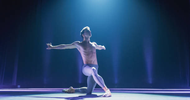 wide cinematic shot of athletic man dancing and rehearsing on classic theatre stage with dramatic lighting. graceful classical ballet male dancer performing his choreography professionally - theatrical performance ballet stage theater dancing imagens e fotografias de stock