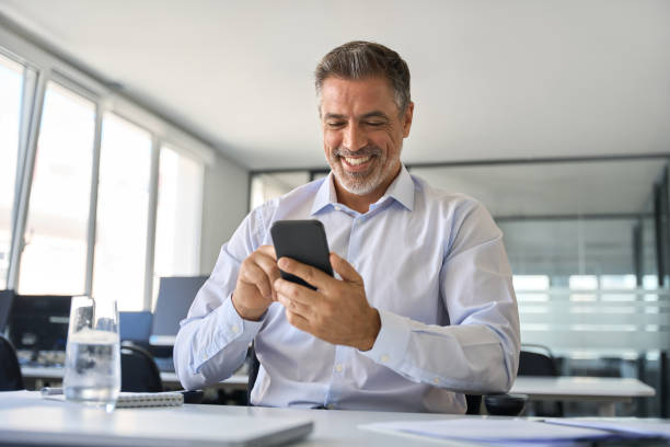 istock Happy mid aged business man executive using mobile phone at work in office. 1560352077