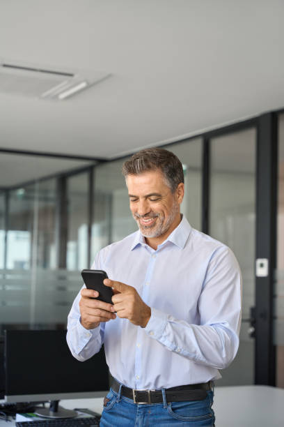 istock Happy mature business man executive standing in office using mobile phone. 1560354747