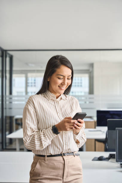 istock Happy professional Asian business woman using mobile phone in office, vertical. 1560354749