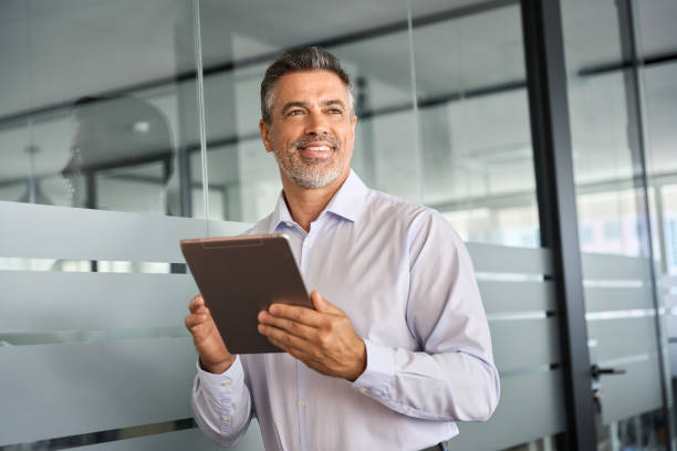 istock Happy mid aged business man manager looking away in office using digital tablet. 1560354766