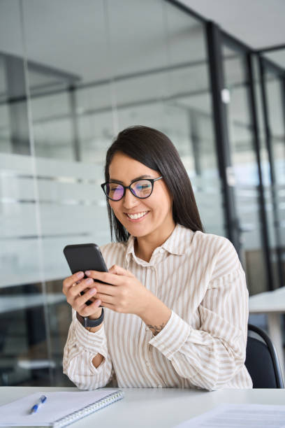 istock Happy Asian female employee using cell phone working in office. 1560355843