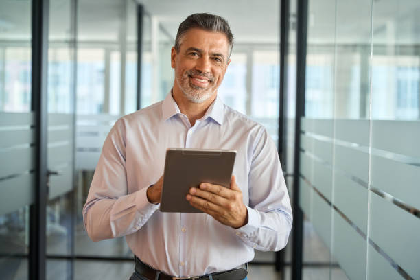 istock Happy mature business man manager standing in office using digital tablet. 1560355845
