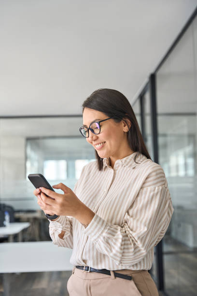 istock Happy Asian business woman worker using mobile phone in office, vertical. 1560355873