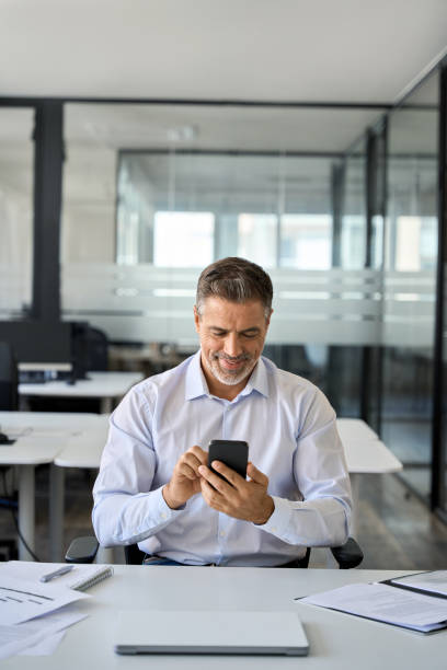 istock Happy mid aged business man manager using cell phone at work in office. 1560358028