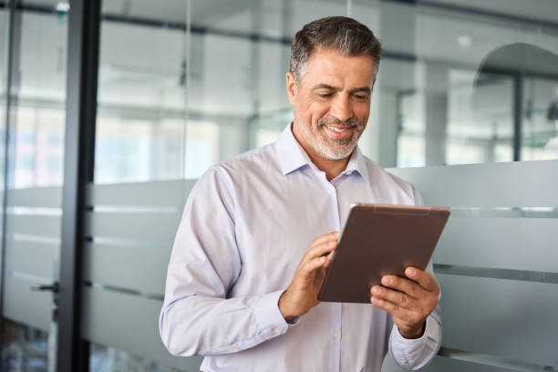 istock Smiling busy mature male manager using tablet standing in office. 1560358580