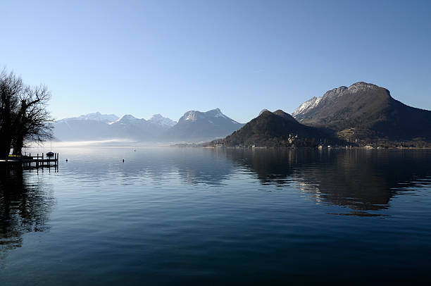 Annecy lake and mountains, view from Talloires, on morning with some mist and reflections in water