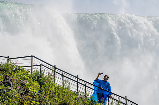 Niagara Falls. USA, 25th August 2022 - A man taking a selfie in front of the strong rapids of Niagara Falls